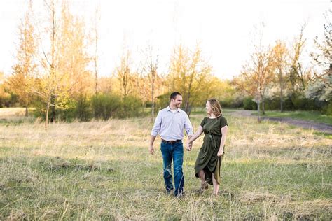 Couple Walking Through Open Field Park At Sunset For Engagement Spring