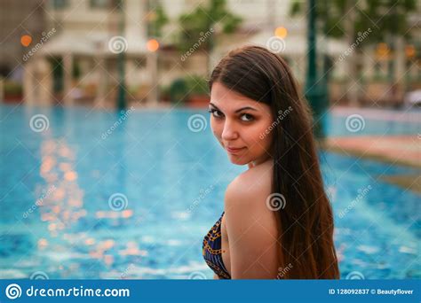 Portrait Of Woman Sitting On Edge Of Swimming Pool Wearing Bikini
