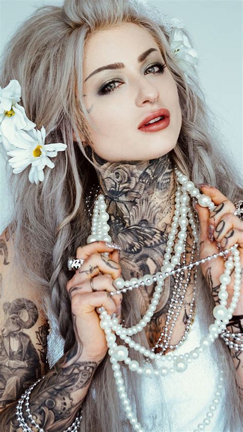 A Woman With Tattoos And Pearls On Her Neck Is Posing For The Camera While Wearing A White Dress