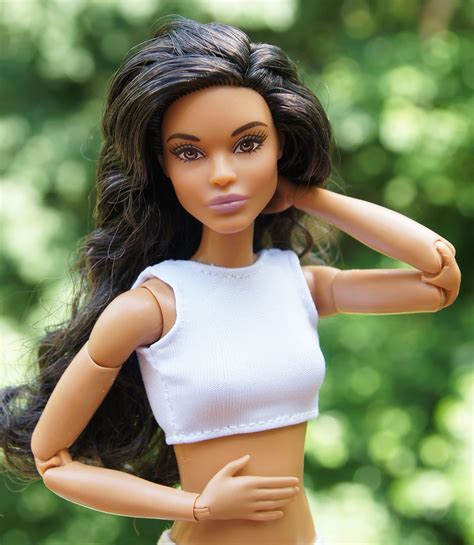 A Close Up Of A Doll Wearing A White Top And Shorts With Trees In The