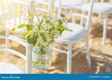 White Chairs At A Beach Wedding Ceremony Decorated With A Hanging Jar