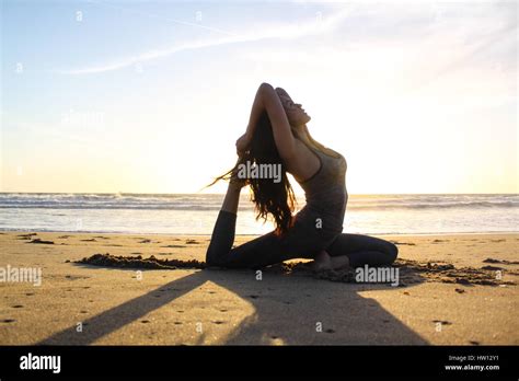 Beautiful Woman Doing Yoga On The Beach During Sunset Stock Photo