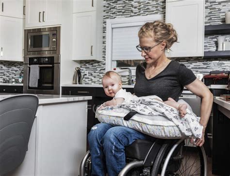 A Paraplegic Mother Holding Her Baby On Her Lap In Her Kitchen While