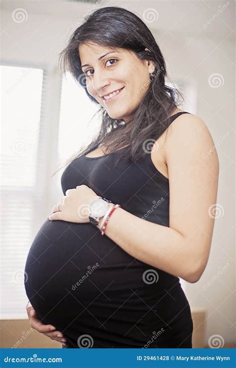 A Pregnant Indian Woman Smiling At The Camera And Standing Against A