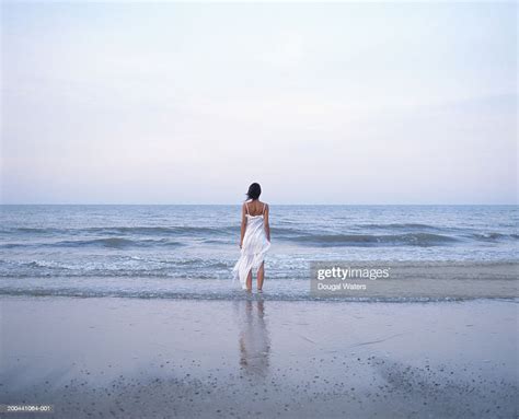Young Woman On Beach Wearing White Dress Facing Ocean Rear View High