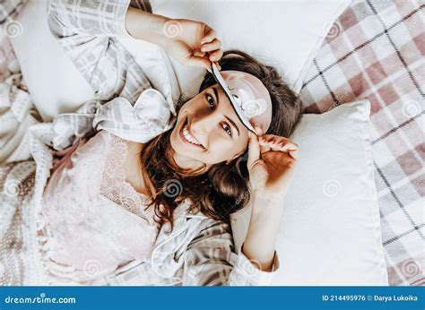 a sleepy brunette girl lies in bed with a blindfold waking up in the morning cozy home morning