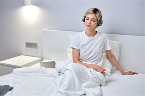 Female In Domestic Wear Listening To Music In Headphones Sit On Bed