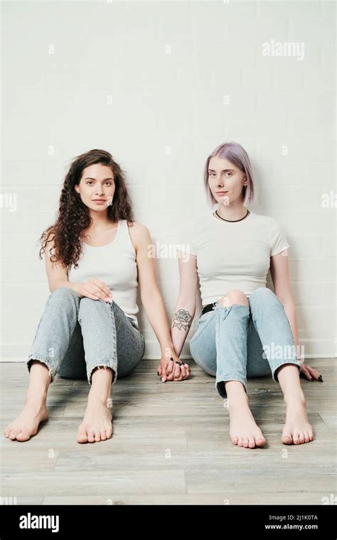 Portrait Of Content Young Caucasian Lesbians In Jeans Sitting On Floor