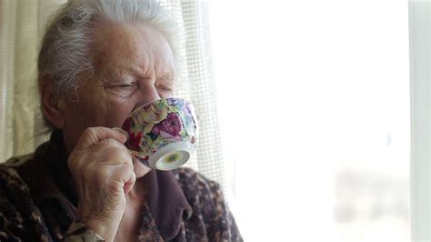 Old Serious Woman Drinking Tea And Looking Out The Window Concept Of Aging And Loneliness In
