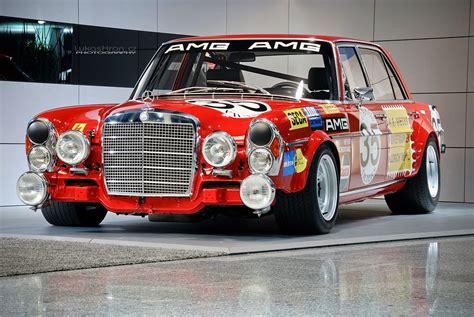 An Old Red Race Car Parked In Front Of A Wall With The Name Ams Amg On It