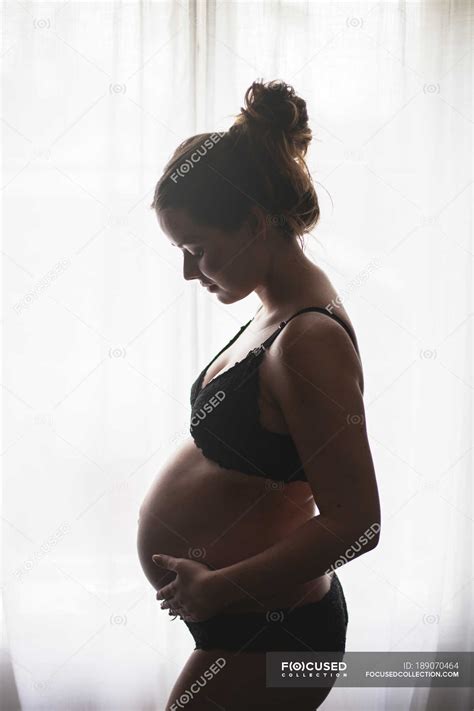 Side View Of Pregnant Woman Standing By Window Indoors Mum Stock Photo