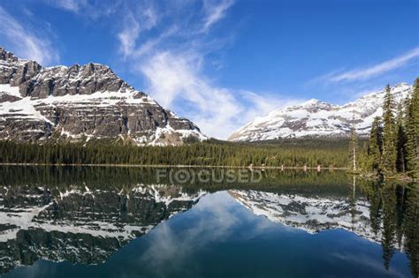 View Of Lake Ohara With Mountains And Trees Under Blue Cloudy Sky At