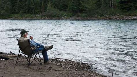 Man Sitting In A Folding Chair On The Bank Of A Large River In Alaska