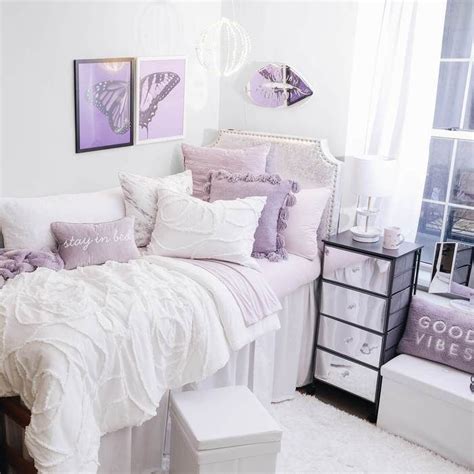 a white bed sitting next to a window covered in purple and white pillows on top of it