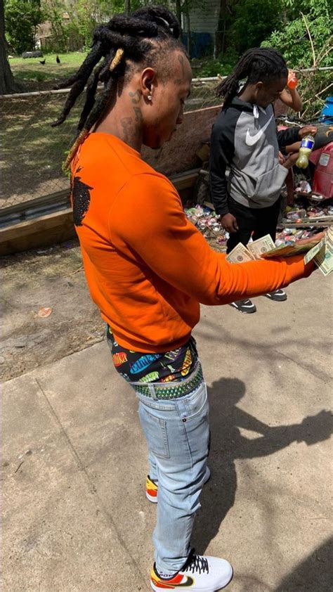 a man with dreadlocks and an orange shirt is handing money to another person