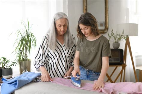 Teenage Girl Ironing And Helping With Household Chores Her Senior Grandmother At Home Stock