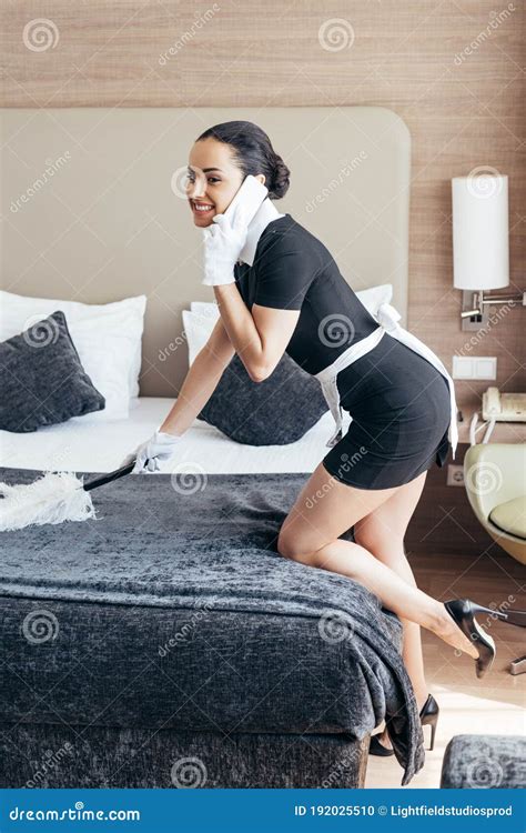 Pretty Maid In White Gloves Cleaning Bed With Duster And Talking On