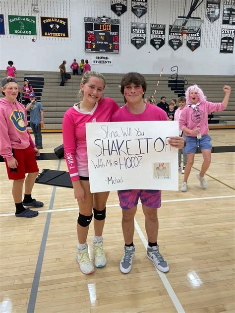 Two Girls In Pink Shirts Holding Up A Sign That Says Shake It To Whats