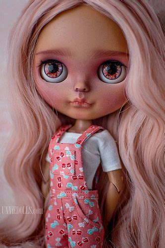 A Doll With Long Blonde Hair And Blue Eyes Wearing Pink Overalls