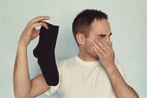 Man Grips Nose With Fingers Holding A Smelly Sock In Hand Stock Photo