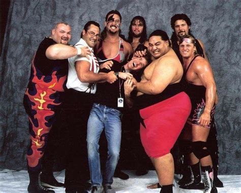 A Group Of Men Standing Next To Each Other In Front Of A Gray Background With The Wrestler