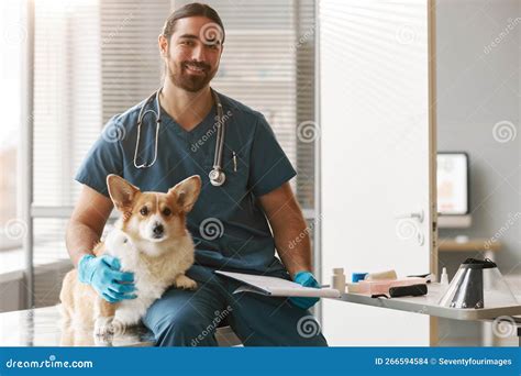 Young Successful Veterinarian In Uniform Sitting By Workplace In