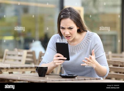 Angry Girl Looking At Her Smart Phone Annoyed On A Restaurant Terrace