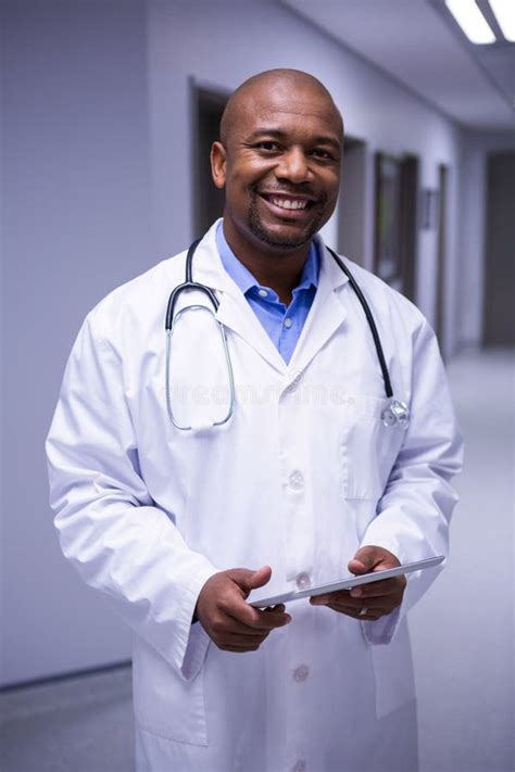Portrait Of Male Doctor Standing With Digital Tablet In Corridor Stock