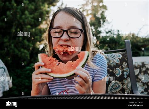 Girl wearing eyeglasses eating watermelon while sitting on chair