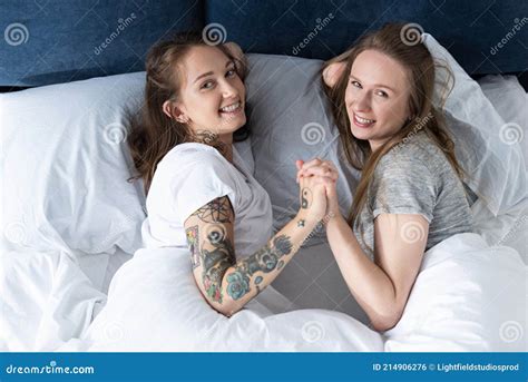 Two Laughing Lesbians Holding Hands While Lying On Bed In Morning Stock Photo Image Of