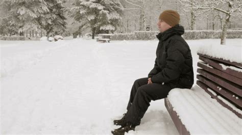 A Young Man Sits On A Bench In Winter Park And Admiring