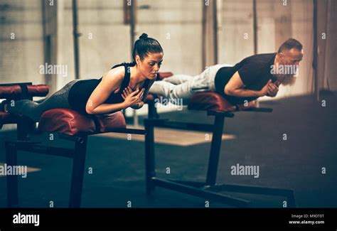 Two Fit People Focused On Doing Core Exercises On Workout Benches