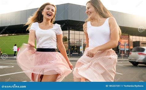 portrait o two cheerful laughing girls in pink skirt running and jumping on car parking at