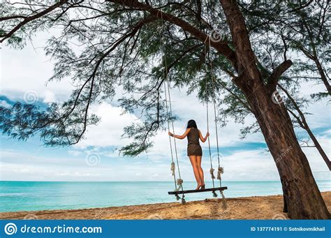 Young Woman Standing On Rope Swing On Tropical Sandy Beach
