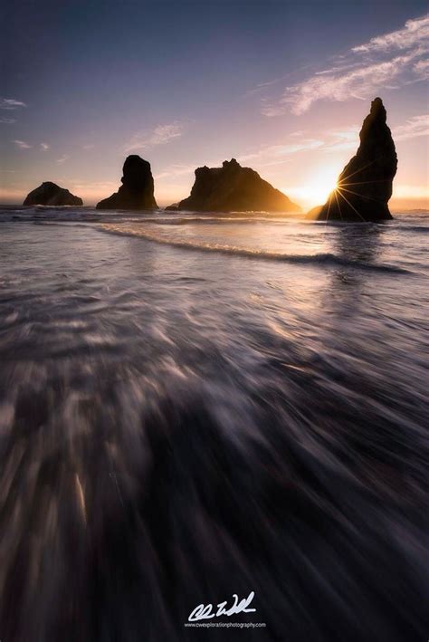 The Sun Is Setting Over Some Rocks In The Water And Waves Are Coming Towards Them