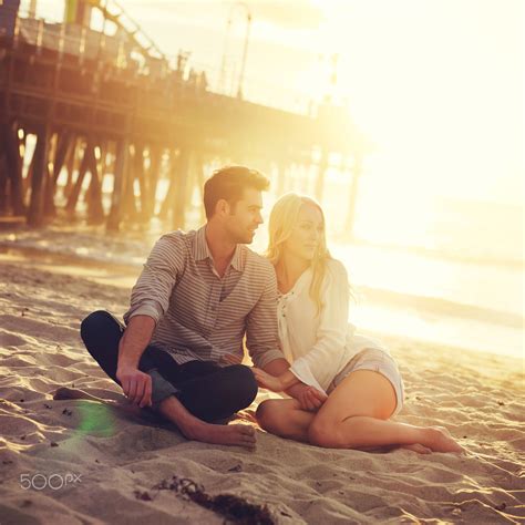 Romantic Couple Sitting On Beach With Golden Sunset By Beach Romantic