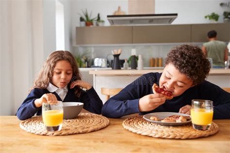 Children Wearing Uniform In Kitchen Eating Breakfast Before Going To