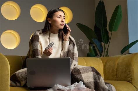 Sick Asian Woman Holds Medicine Sits On The Couch Makes A Video Call On The Phone Consults