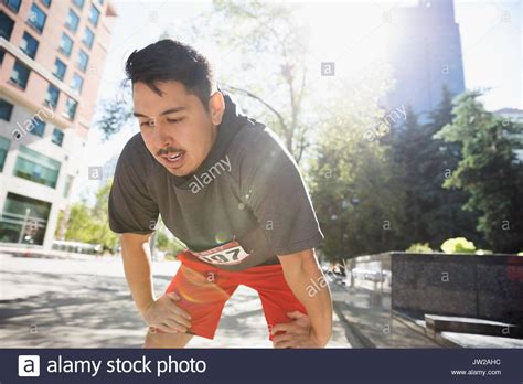 Tired Male Marathon Runner Resting With Hands On Knees On Sunny Urban