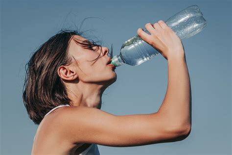 A Girl Drinks Water From A Plastic Bottle On A Blue Sky Background