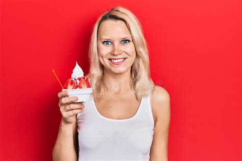 Beautiful Caucasian Blonde Woman Eating Strawberry Ice Cream Looking Positive And Happy Standing