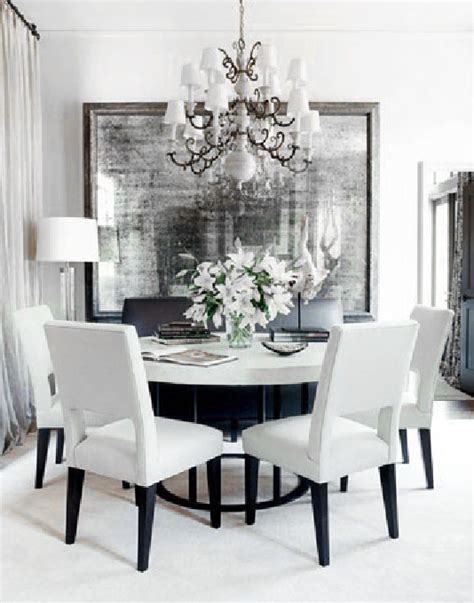 Sophisticated dining room with gray walls features a round wood antique dining table, white and heather gray french dining chairs with silver nailhead trim atop a white rug, white and pink abstract art over a gold leaf bar cart, window with blue and white roman shades and cream buffet cabinet. Dove Gray Home Decor ♅ white and grey dining room | Dining ...