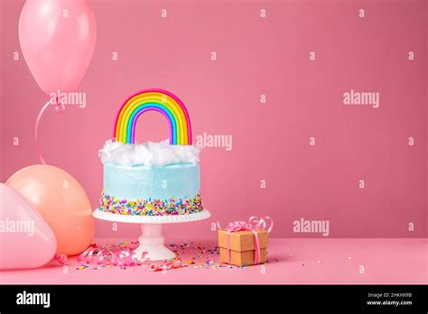 Pastel de cumpleaños azul con dulces de algodón y un colorido arco iris sobre un fondo rosa