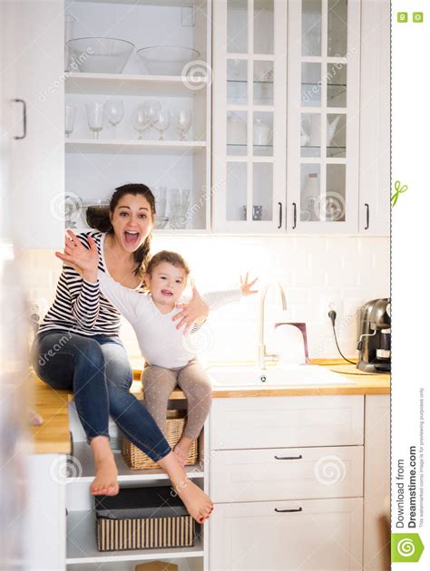 Mother With Daughter In The Kitchen Sitting On Countertop