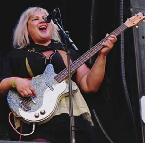 A Woman Singing Into A Microphone While Holding A Guitar In Front Of