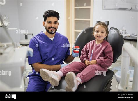 Happy confident male dentist tells little child girl how to brush the