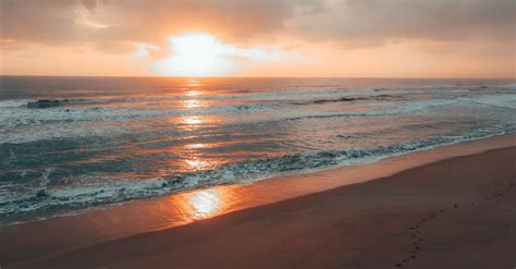 Foamy Sea Waving Near Sandy Beach Against Cloudy Sundown Sky · Free