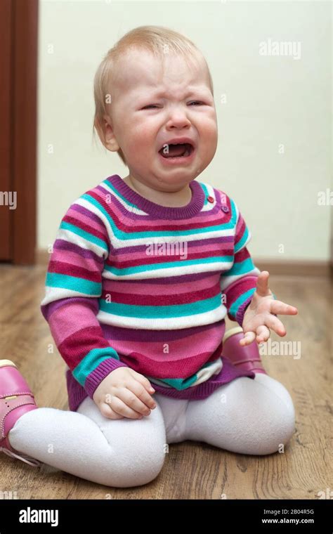 Portrait Of Crying Baby Girl Sitting On The Floor In Pink Dress Stock