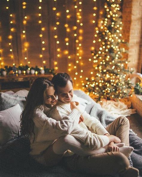 A Man And Woman Sitting On A Bed In Front Of A Christmas Tree With Lights