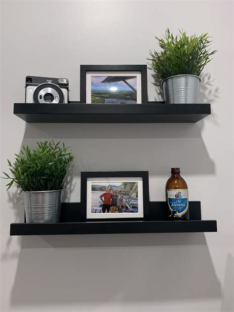 Two Black Shelves With Pictures And Plants On Them One Is Holding A